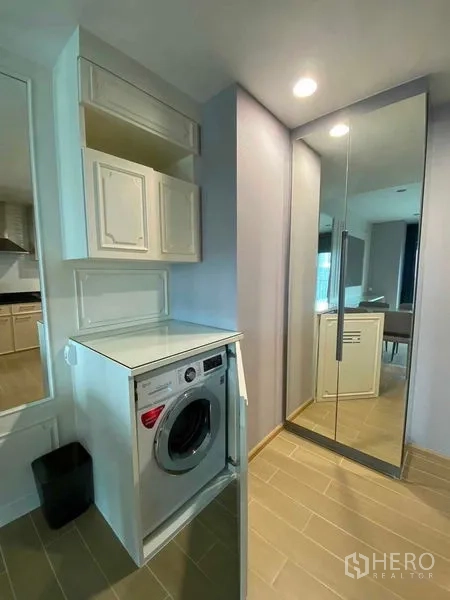 Condominium for rent in Khlong Toei, Bangkok - Laundry niche with front-loading washing machine, storage cabinets and mirrored closet.