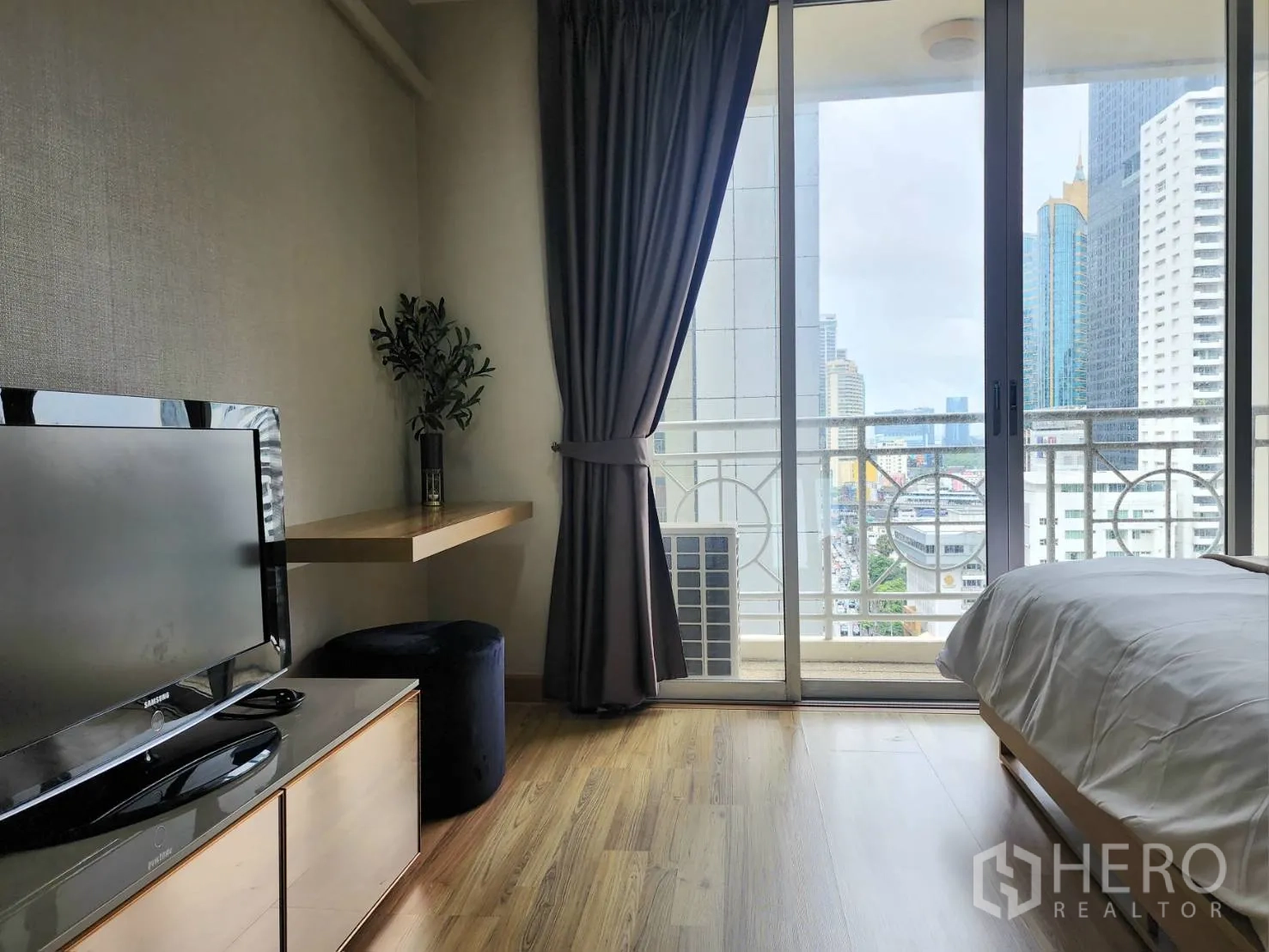 公寓 for rent in Watthana, Bangkok - 卧室一角设电视与壁挂书桌，推拉门通向阳台并见城市景观。