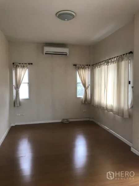 Detached House for rent in Lat Krabang, Bangkok - Spacious master bedroom with wood floors, multiple windows, curtains and wall-mounted air conditioner.