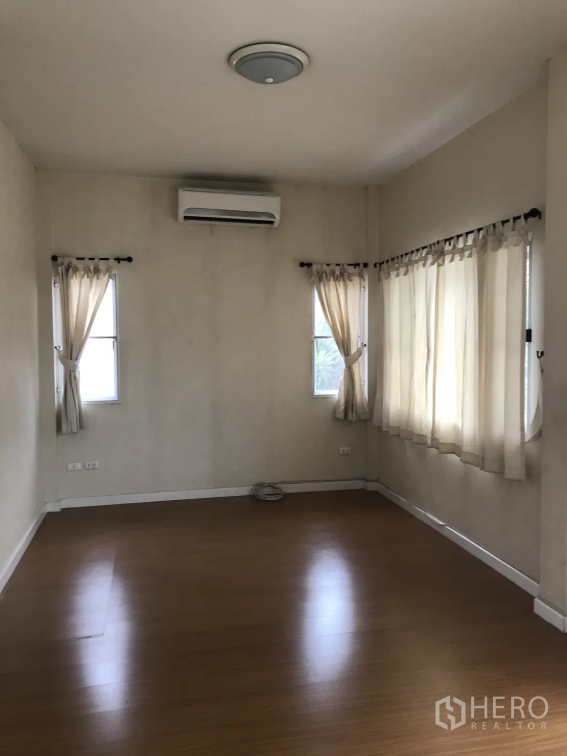 Detached House for rent in Lat Krabang, Bangkok - Spacious master bedroom with wood floors, multiple windows, curtains and wall-mounted air conditioner.