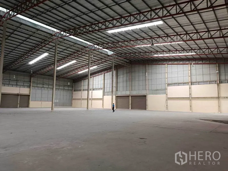 Factory for rent in Samut Prakan - Expansive factory warehouse in Bang Phli with high steel-truss ceiling, bright strip lighting, concrete floor and multiple roller-shutter bays.