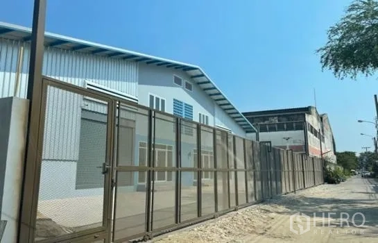 Warehouse for rent in Prawet, Bangkok - Street view of secure warehouse with high metal fence, roller doors and parking apron.