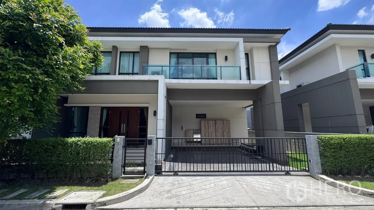 Detached House for rent or sale in Saphan Sung, Bangkok - Modern two‑storey detached house in Saphan Sung, Bangkok with gated driveway, carport and glass balcony framed by hedges under blue sky.