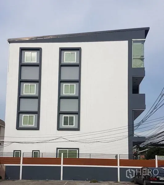 Home Office for sale in Lat Phrao, Bangkok - Side view of a contemporary white building with boxed windows and a sloped roof.