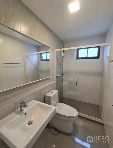 Townhouse for rent in Bang Phli, Samut Prakan - Modern bathroom with glass shower enclosure, window, large mirror, sink and toilet.