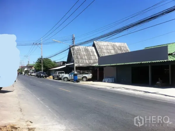 Warehouse for rent in Lam Luk Ka, Pathum Thani - Street view in Lam Luk Ka showing low-rise warehouses and shopfronts along a paved road with clear blue sky.