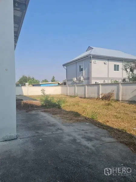 工厂 出租或出售在Lam Luk Ka, Pathum Thani - 建筑后院空地，与相邻住宅之间的围墙。