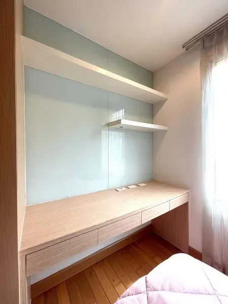 Condominium for rent - Bright study nook with a long wooden desk, floating shelves and a softly curtained window.