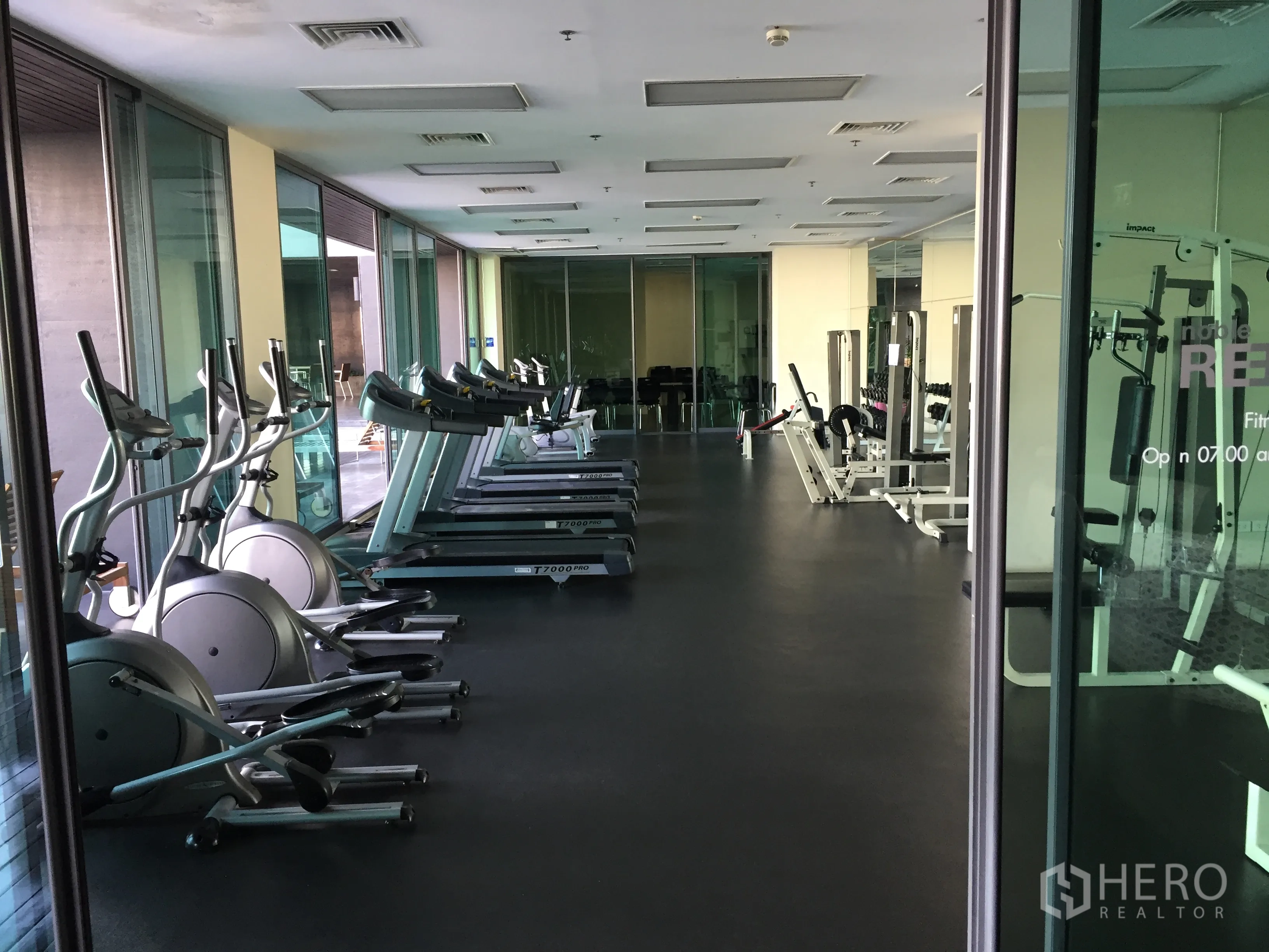 Condominium for rent or sale in Khlong Toei, Bangkok - Glass-walled fitness center featuring treadmills, ellipticals, and weight machines in a Bangkok condo.