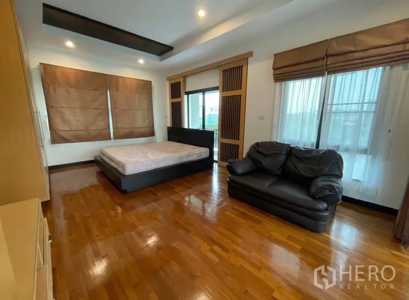Detached House for rent in Chatuchak, Bangkok - Spacious master bedroom with wood floors, sofa and access to a balcony.