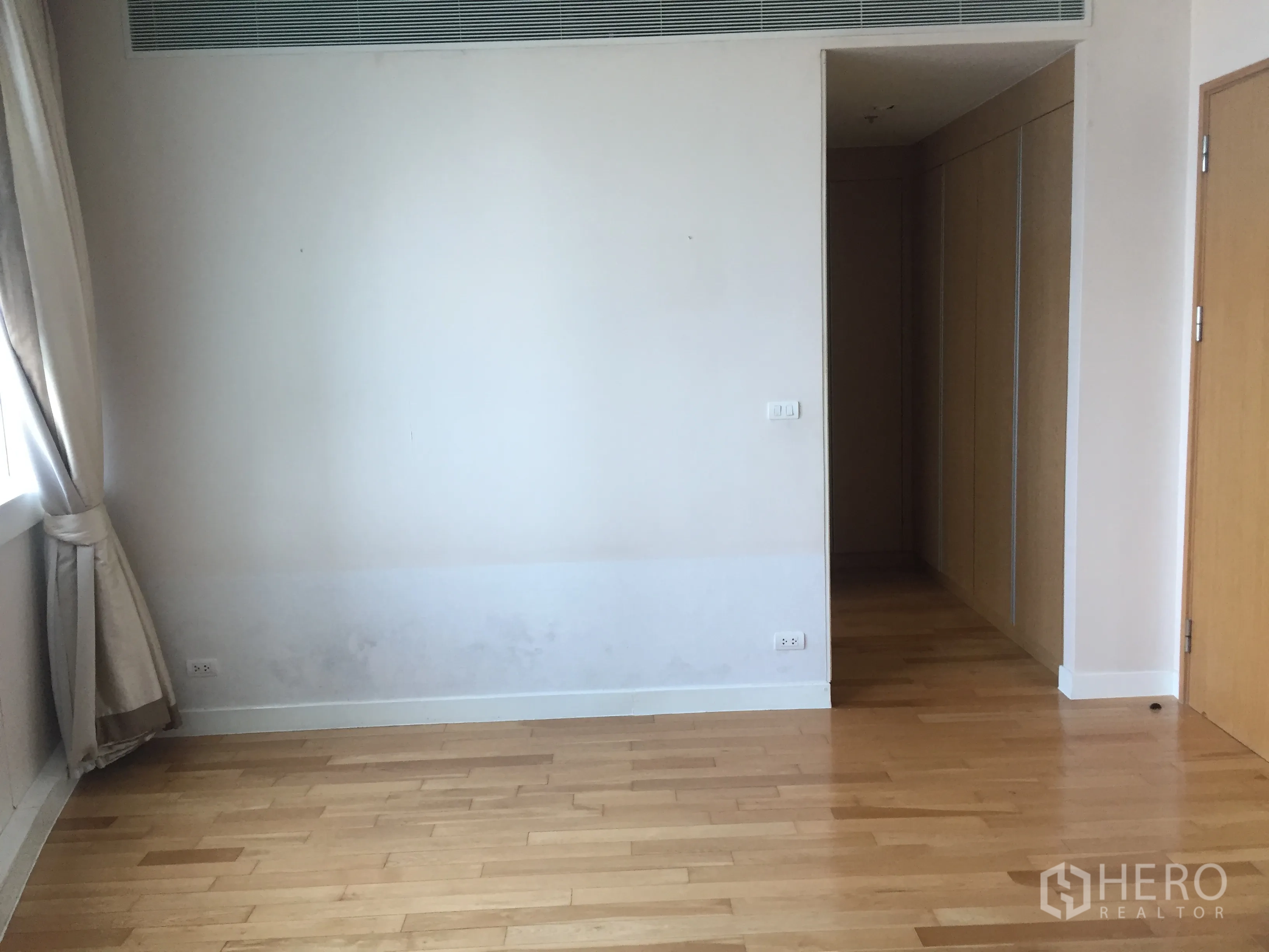 Condominium for rent in Khlong Toei, Bangkok - Spacious bedroom with hardwood flooring, natural light, and corridor to closets.