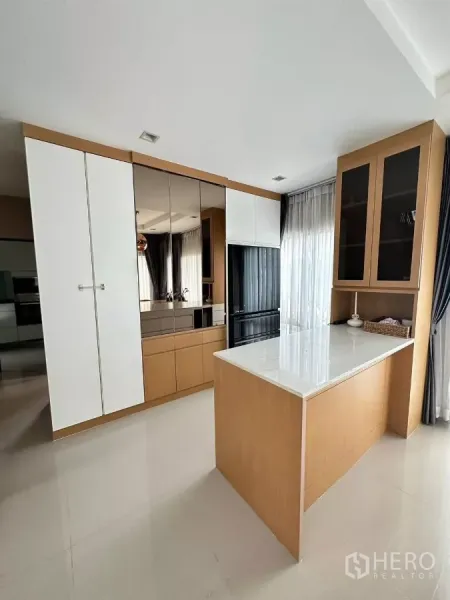 Detached House for rent in Saphan Sung, Bangkok - Kitchen island and custom cabinetry with glass-front cupboards by wide windows.