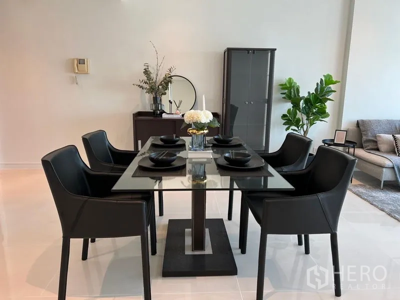 Condominium for rent in Watthana, Bangkok - Close-up of the dining set with six black chairs around a glass table, centerpiece flowers, and a storage cabinet.