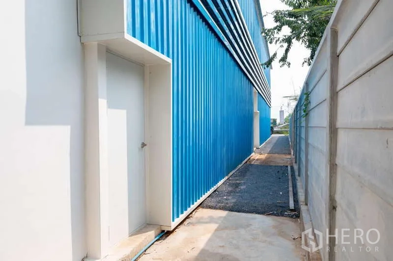 货栈 出租在Khlong Luang, Pathum Thani - 仓库侧边狭长通道，白色服务门与围墙。