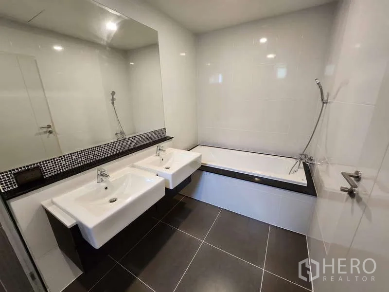 Detached House for rent in Wang Thonglang, Bangkok - Contemporary bathroom with double basins, large mirror, bathtub and handheld shower on dark tiled floor.