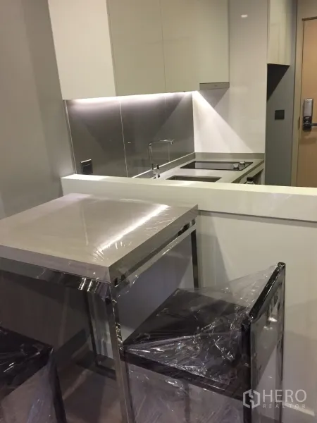 Condominium for rent in Watthana, Bangkok - Compact kitchen with induction hob, under-cabinet lighting and a breakfast bar with stools.