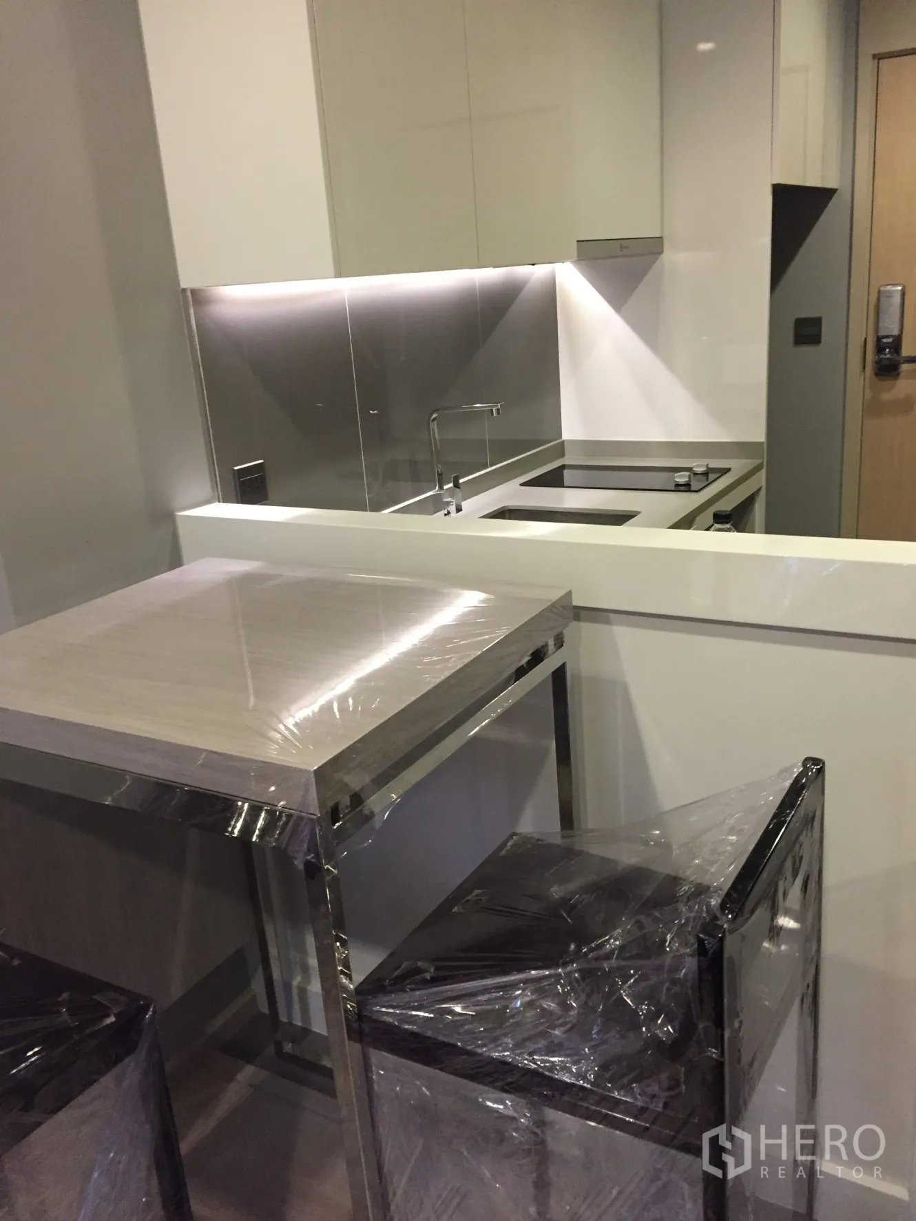 Condominium for rent in Watthana, Bangkok - Compact kitchen with induction hob, under-cabinet lighting and a breakfast bar with stools.
