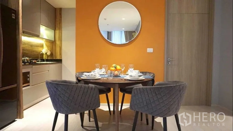 Condominium for rent in Pathum Wan, Bangkok - Cozy dining nook beside an orange feature wall adjacent to a modern fitted kitchen.