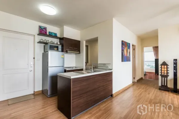 Condominium for rent in Bang Na, Bangkok - Entrance and open kitchen with wood cabinetry, breakfast counter, and hallway to bedrooms.