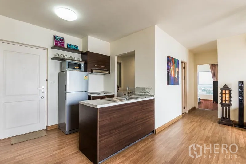 Condominium for rent in Bang Na, Bangkok - Entrance and open kitchen with wood cabinetry, breakfast counter, and hallway to bedrooms.