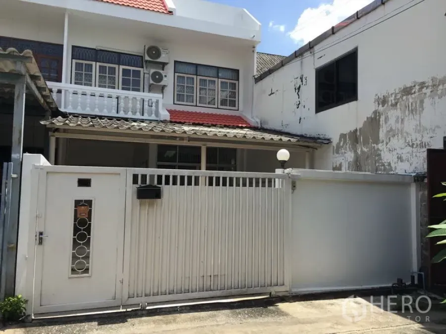 联排别墅 出租在Phra Khanong, Bangkok - 两层联排别墅外立面，白色庭院门、阳台与红色屋瓦。