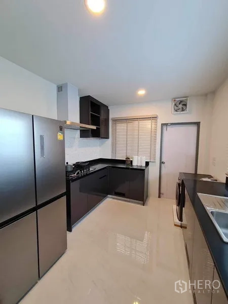 Detached House for rent or sale in Bang Phli, Samut Prakan - Bright kitchen with black cabinetry, gas hob, stainless fridge and white tiled backsplash.