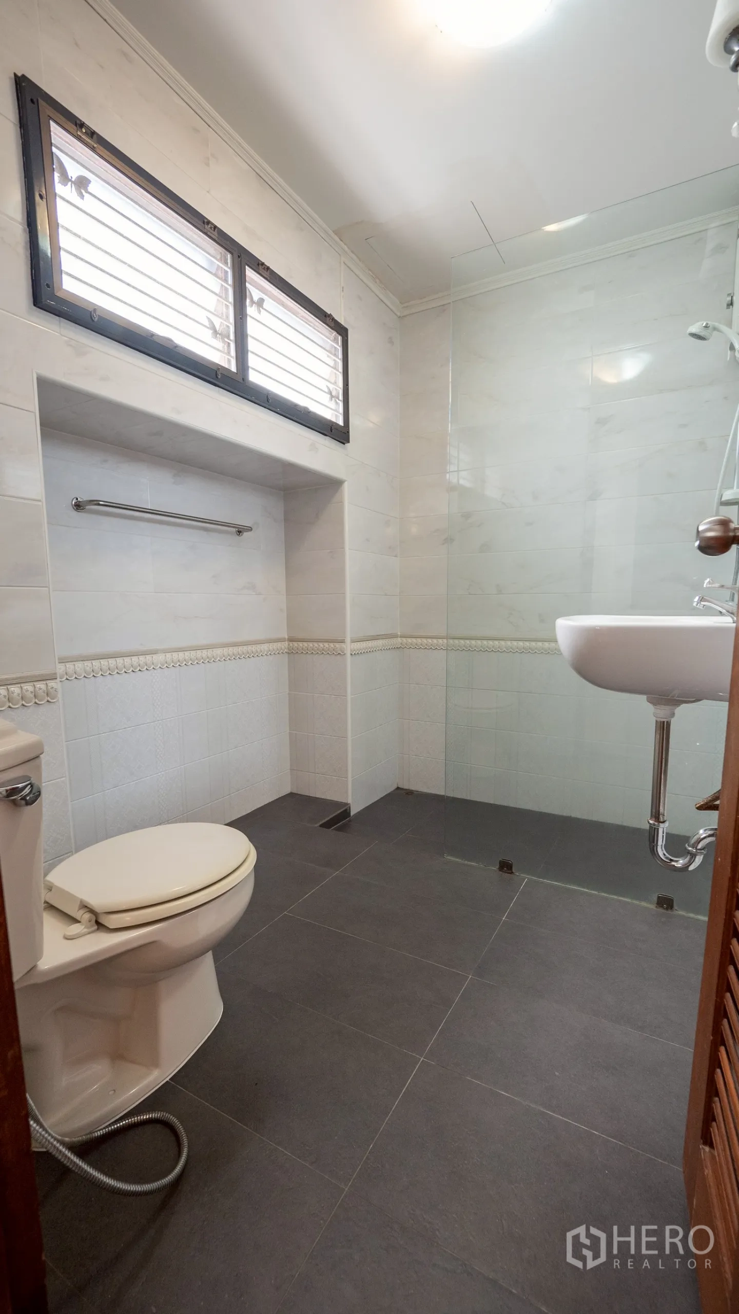 Townhouse for rent in Khlong Toei, Bangkok - Bathroom with frosted sliding shower door, black counter and white tiles.