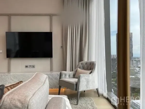 Condominium for rent in Watthana, Bangkok - Cozy reading chair by a panoramic window next to a wall-mounted TV and marble ledge.