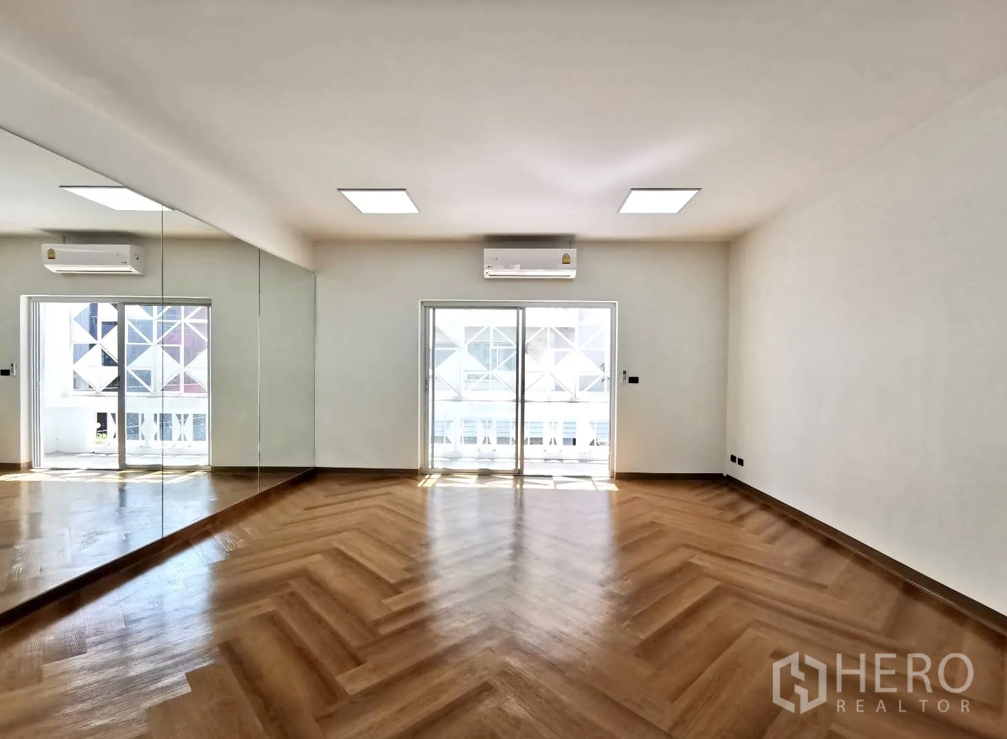 Home Office for rent in Watthana, Bangkok - Large room with full-height mirror, herringbone floors, air conditioning and balcony access through sliding doors.