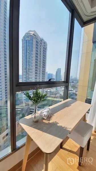 公寓 出租在Khlong Toei, Bangkok - 转角落地窗书桌，俯瞰澎蓬区域的城市天际线。