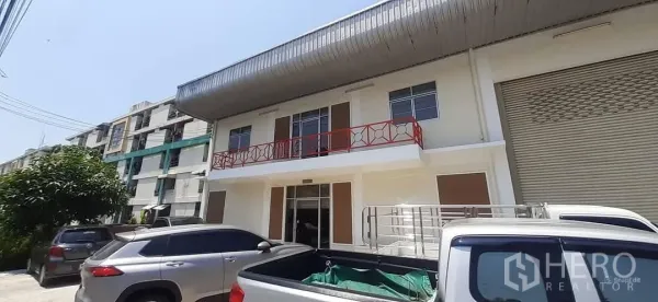 Factory for rent in Bang Sao Thong, Samut Prakan - Renovated factory frontage with red balcony railing, roller shutter door and parking bays.