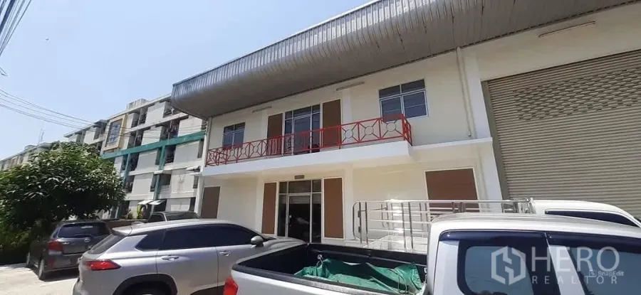 工厂 出租在Bang Sao Thong, Samut Prakan - 翻新工厂外立面，红色阳台栏杆、卷闸门与停车位。
