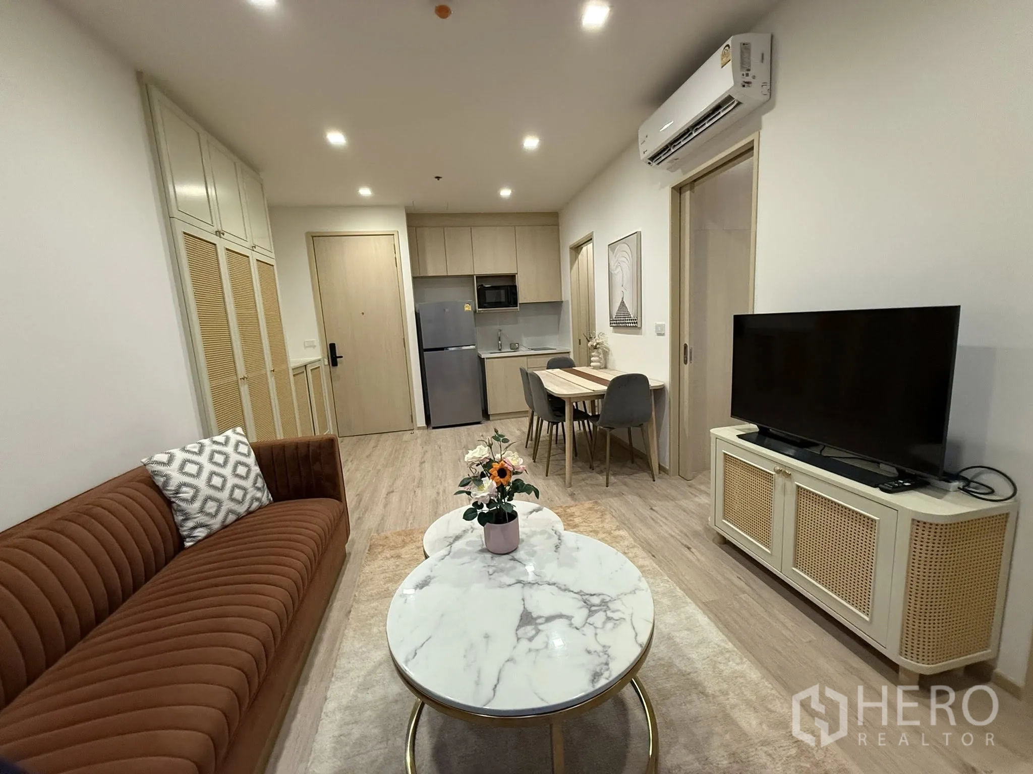 คอนโด for rent in Watthana, Bangkok - ห้องนั่งเล่นมองไปยังครัว มีโซฟาสีน้ำตาล โต๊ะกลางหินอ่อน ตู้วางทีวี ชุดโต๊ะทานอาหาร และครัวขนาดกะทัดรัด