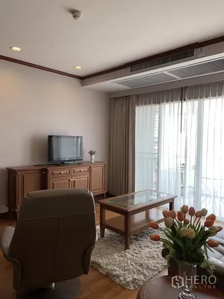 公寓 出租在Khlong Toei, Bangkok - 采光充足的客厅，皮沙发、电视柜与玻璃茶几，推拉门通往阳台，木地板。