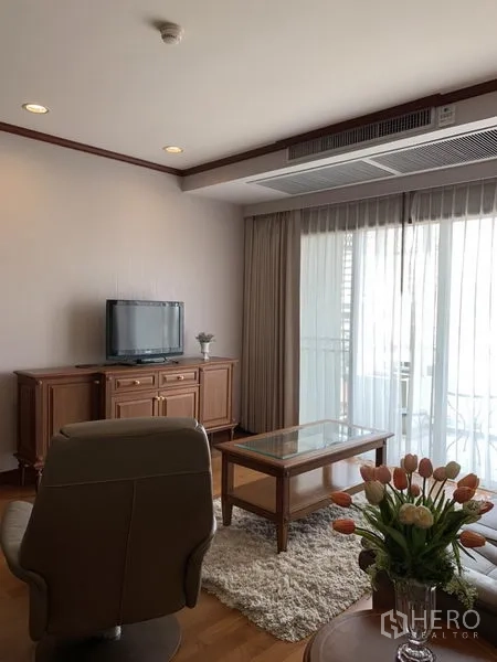 公寓 出租在Khlong Toei, Bangkok - 采光充足的客厅，皮沙发、电视柜与玻璃茶几，推拉门通往阳台，木地板。