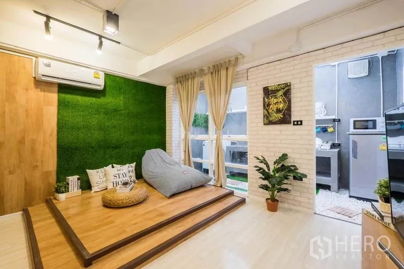 Detached House for rent in Khlong Toei, Bangkok - Warm living room with platform lounge, faux grass wall, sliding door to kitchen and plants.