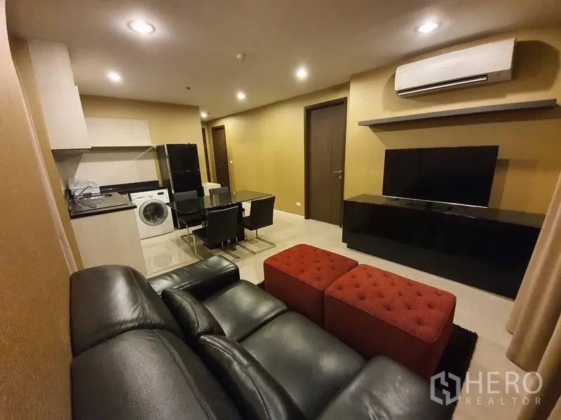 คอนโด ให้เช่าในSathon, Bangkok - มุมนั่งเล่นพร้อมโซฟาหนังสีดำ ที่วางเท้าสีแดง ทีวีแขวนผนัง ชุดทานอาหาร และครัวย่อมพร้อมเครื่องซักผ้า