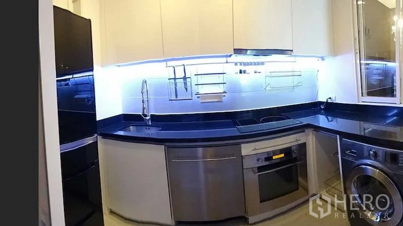 Condominium for rent or sale in Watthana, Bangkok - U-shaped kitchen featuring black stone countertops, stainless appliances and LED backsplash lighting.