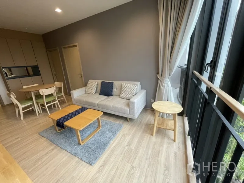公寓 出租在Watthana, Bangkok - 温馨起居区，浅色沙发、茶几与通高窗景绿树。
