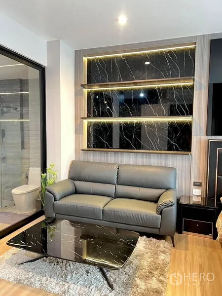 Townhouse for rent in Saphan Sung, Bangkok - Cozy sitting area with leather sofa, illuminated marble accent shelves and a glass door.