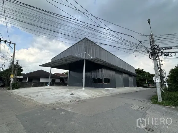 Warehouse for rent in Bang Kapi, Bangkok - Street perspective of the dark metal warehouse with covered dock and outdoor parking.