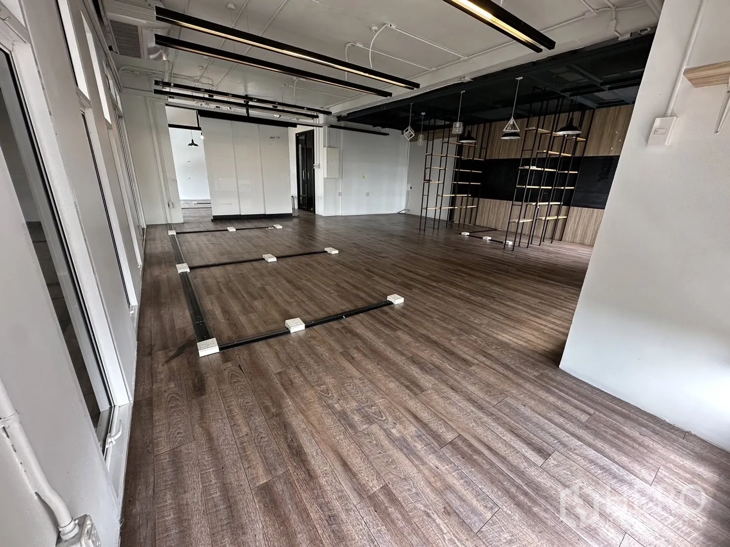 办公室 for rent in Watthana, Bangkok - 大开间办公地面设走线槽与插座，木纹地板、悬挂灯具和带层架的装饰墙。