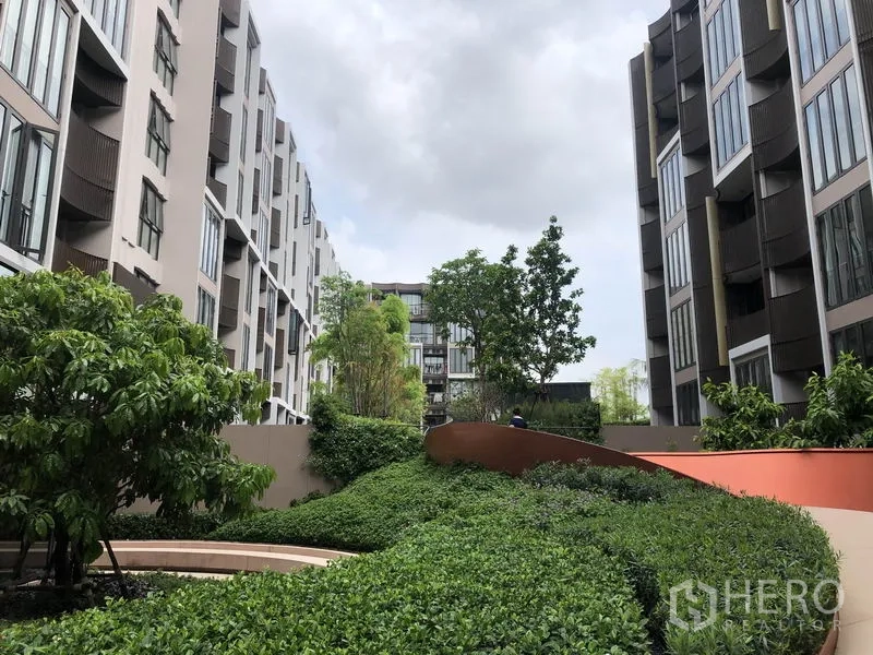 Condominium for rent or sale in Watthana, Bangkok - Landscaped courtyard between low-rise buildings with lush greenery and walkway.