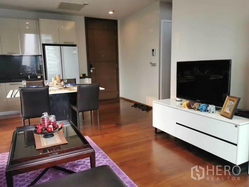 Condominium for rent in Watthana, Bangkok - Living area toward entry with TV console, dining table and kitchen on wood flooring.