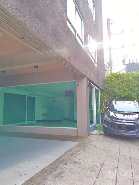 Retail Space for rent - Corner of low-rise building showing glass-front shop and on-site parking bay with car.