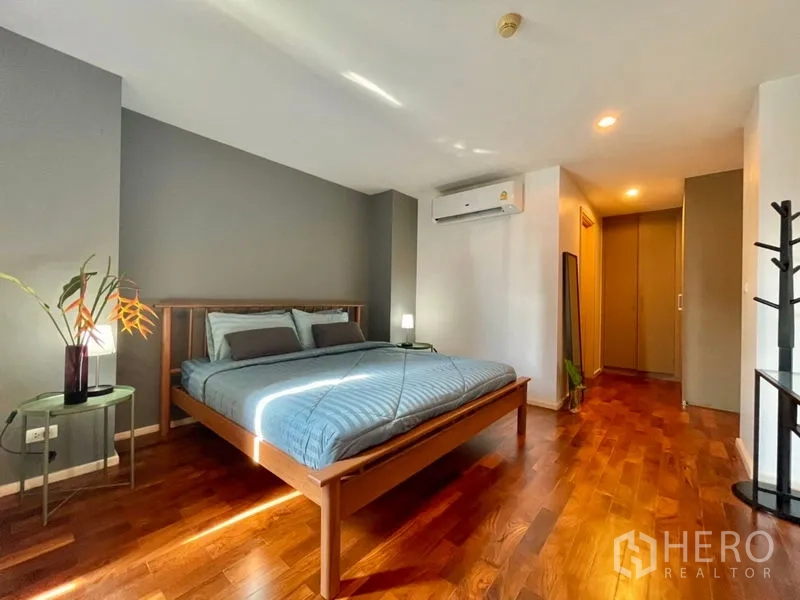 Condominium for rent or sale in Khlong Toei, Bangkok - Spacious master bedroom with wooden bed, accent wall, and polished floors.