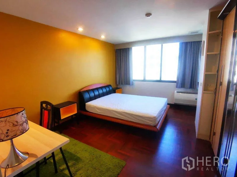 Condominium for rent in Khlong Toei, Bangkok - Bright bedroom with mustard accent wall, double bed, desk and large window on parquet flooring.