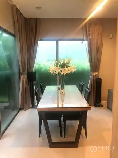 Detached House for rent or sale in Bang Kapi, Bangkok - Dining area with a six-seat table by sliding glass doors and curtains.