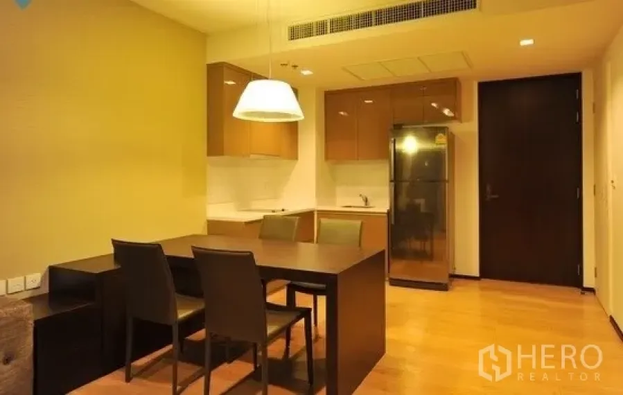 公寓 出租在Khlong Toei, Bangkok - 开放式用餐区，深色餐桌与吊灯，背后连通小厨房