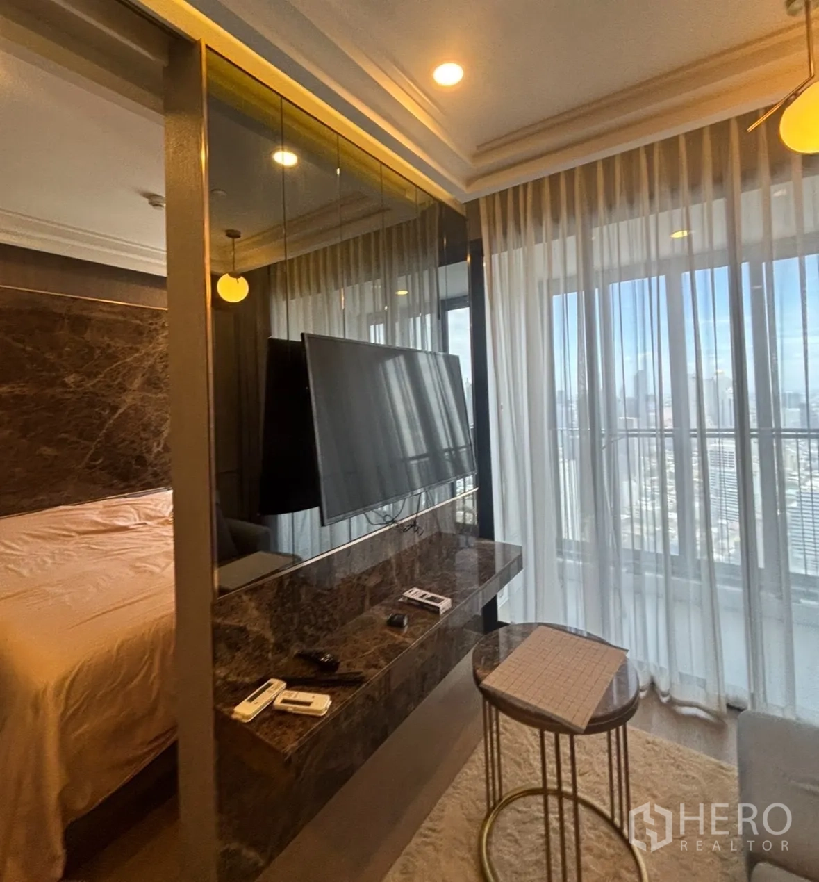Condominium for rent in Bang Rak, Bangkok - TV on a marble console facing the bed, with sheer curtains and large windows to the balcony.